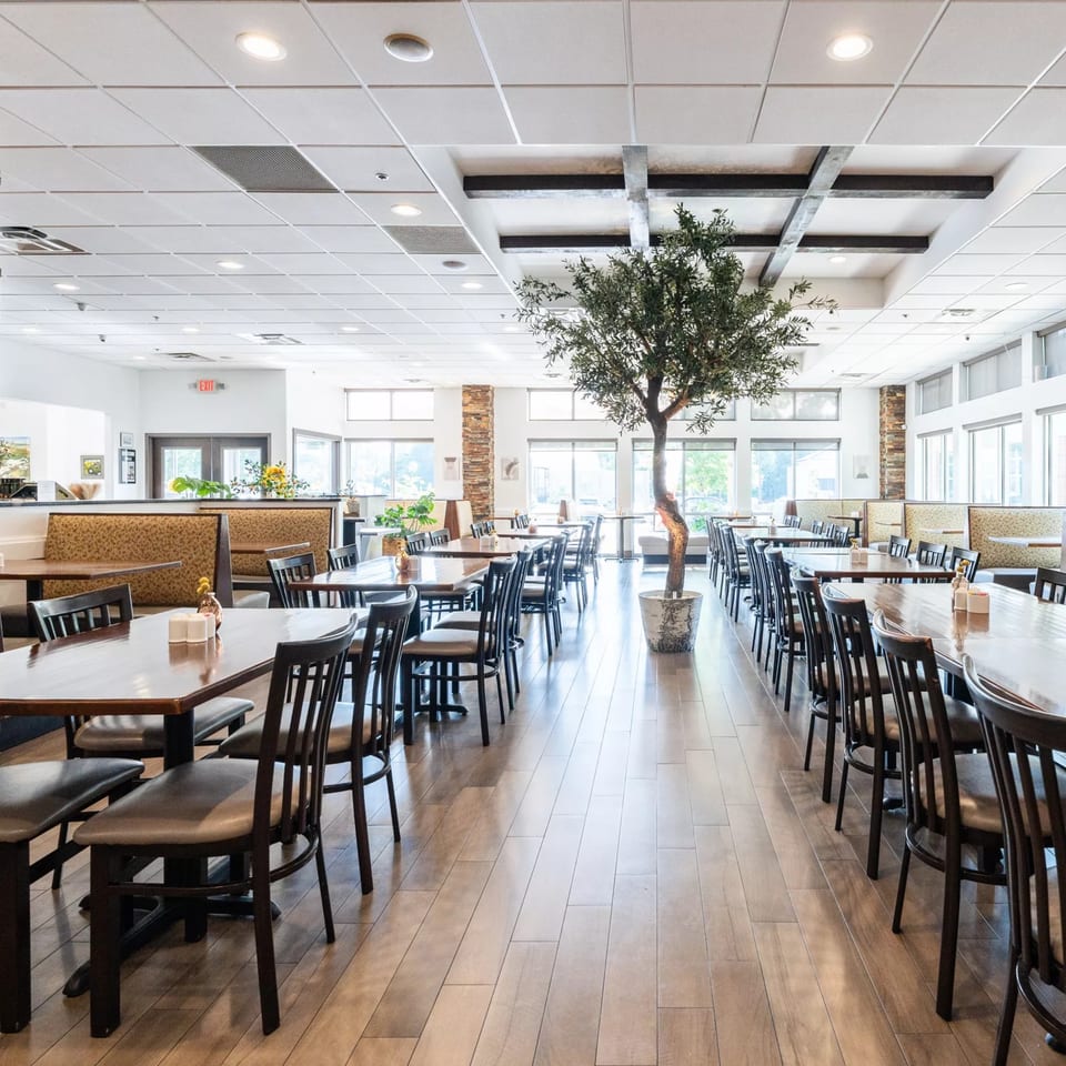 Spacious dining room at Anthony's Restaurant with rows of tables, chairs, booths, and a large olive tree.