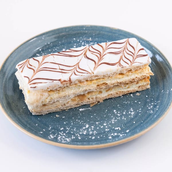 A rectangular Napoleon pastry with white icing and chocolate drizzle, dusted with powdered sugar on a blue plate.