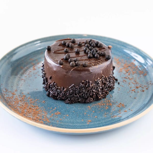 A small, round chocolate cake with chocolate sprinkles and cocoa powder on a blue plate.
