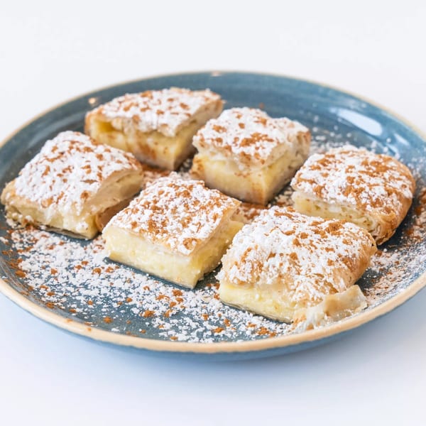 Six pieces of Anthony's Restaurant's dessert, topped with powdered sugar and cinnamon, on a blue plate.