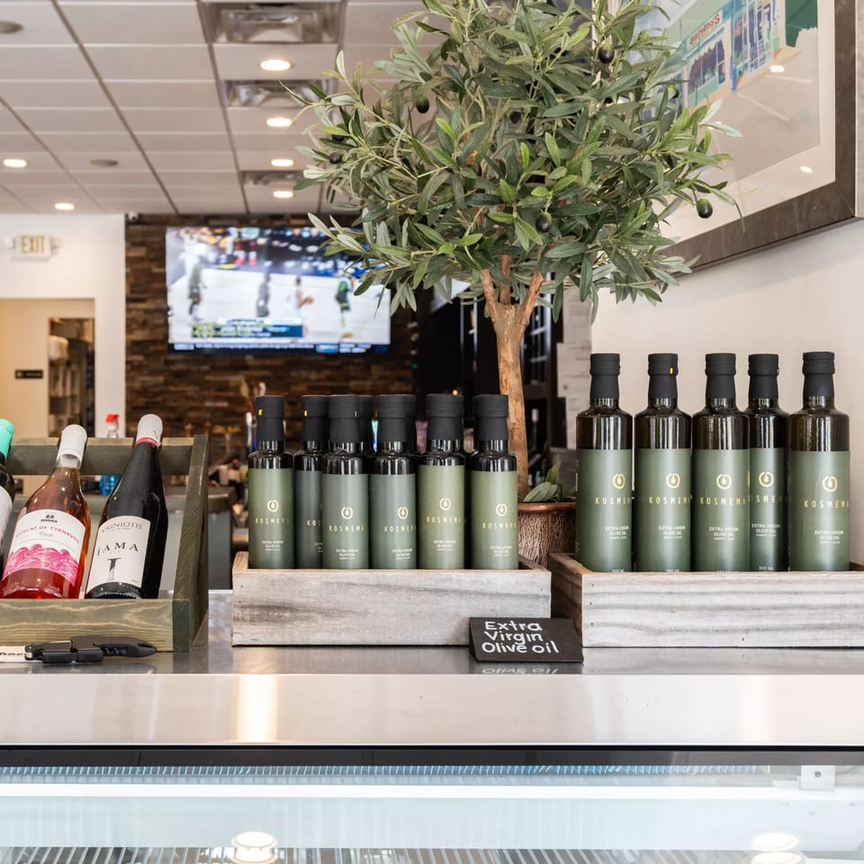 Bottles of Kosmena extra virgin olive oil and wine on a counter with a small olive tree.