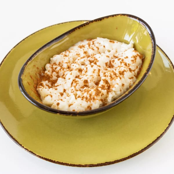 Creamy rice pudding with cinnamon sprinkled on top, served in a green bowl on a matching plate.
