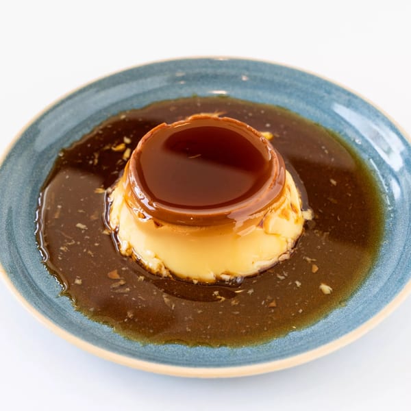 Flan dessert with caramel sauce on a blue plate at Anthony's Restaurant.