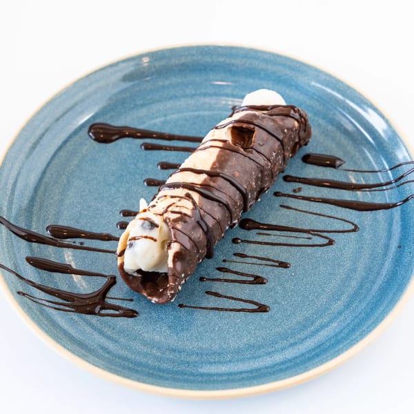 A chocolate-dipped cannoli with white cream filling and chocolate drizzle on a blue plate.