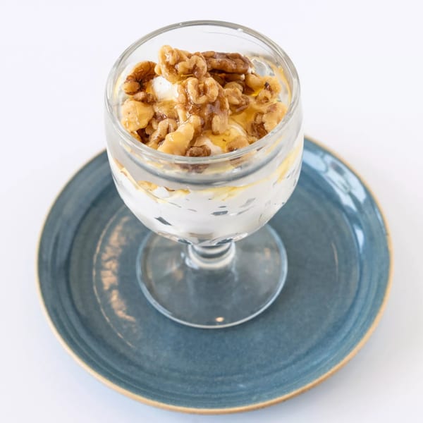 A glass of yogurt topped with walnuts and honey, served on a blue plate.