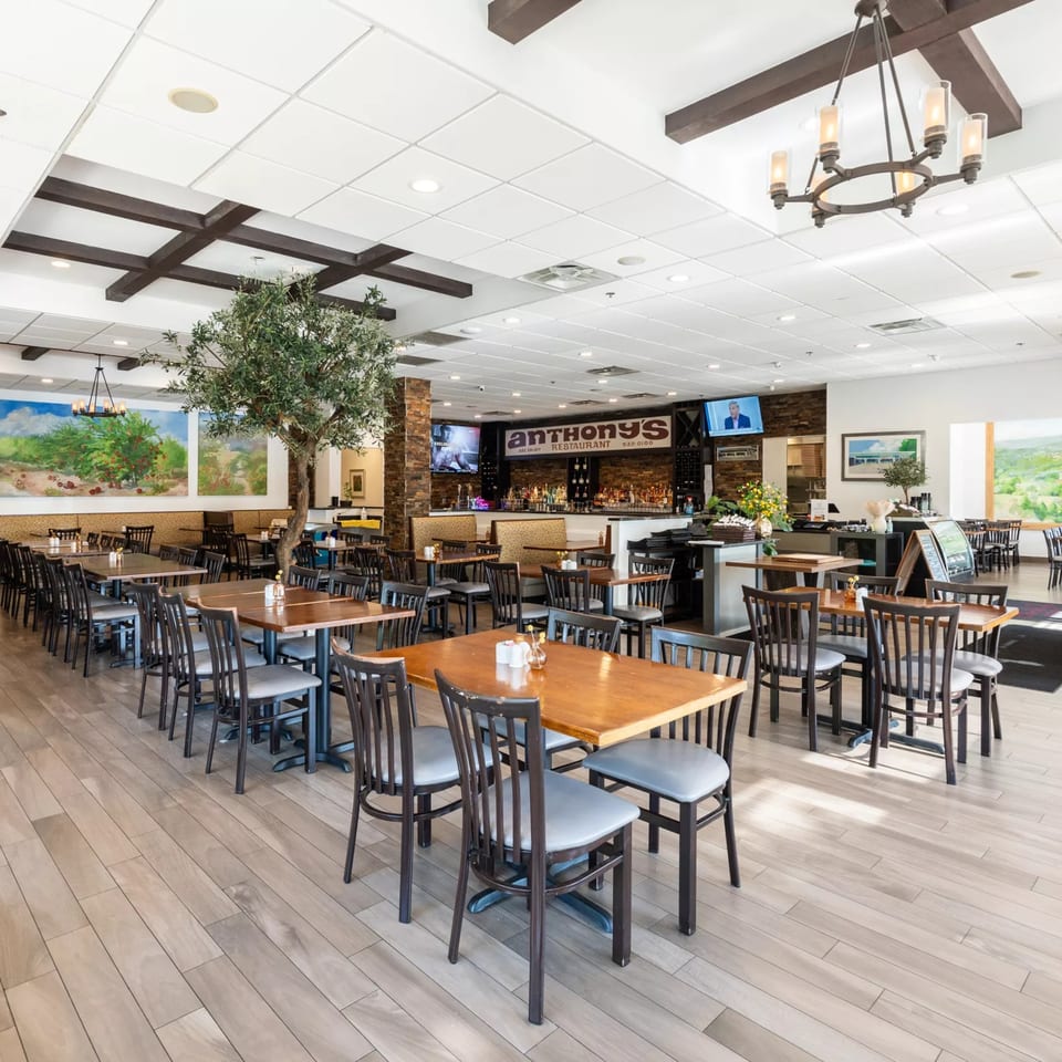 Spacious dining room at Anthony's Restaurant with wooden tables, chairs, a bar, and murals.
