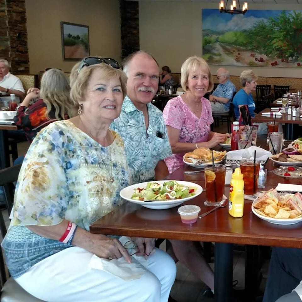 Three smiling diners at Anthony's Restaurant, with salads, sandwiches, and drinks on their table.