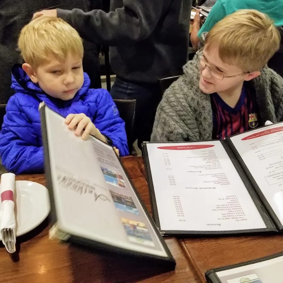 Two young boys at Anthony's Restaurant looking at menus, one in a blue jacket, the other in glasses.