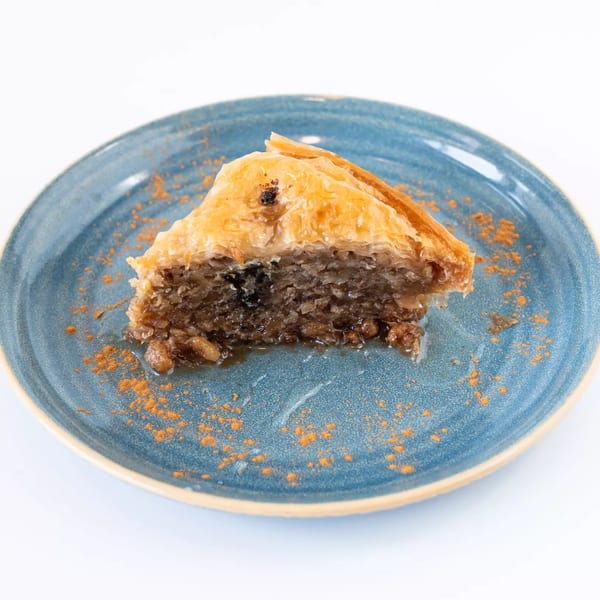 A slice of baklava with a rich nut filling and honey syrup, dusted with cinnamon on a blue plate.